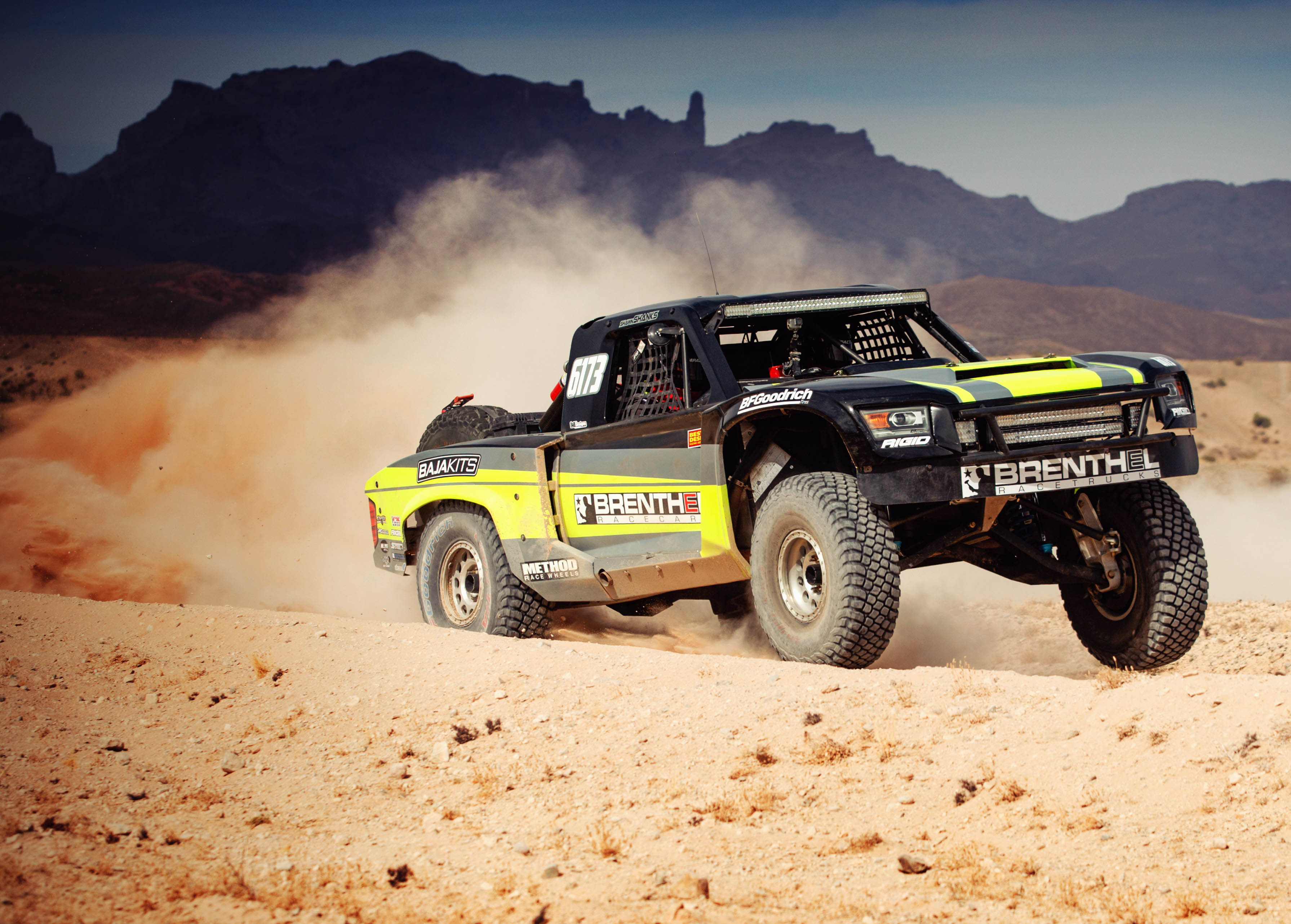 Bi Trophy truck racing on a desert dirt road while leaving behind a large cloud of dust